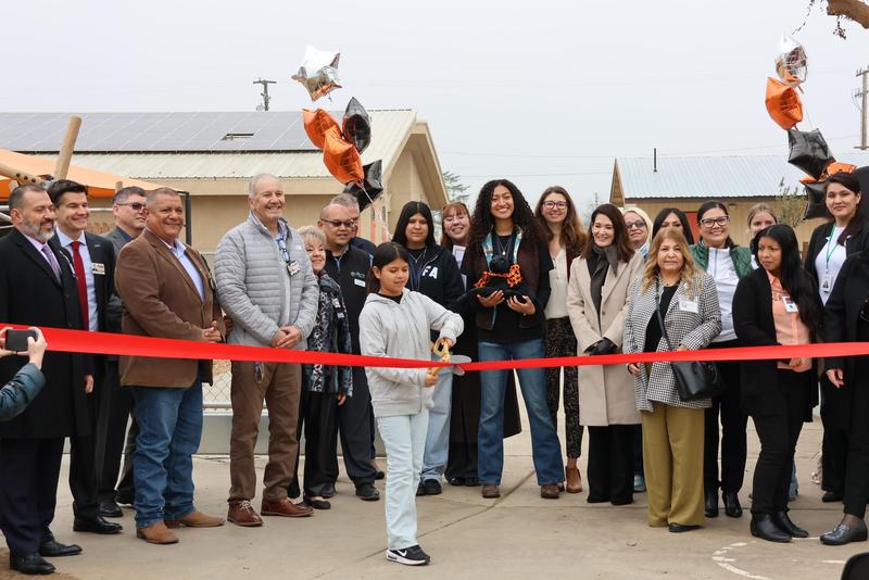 A student cuts the ribbon surrounded by staff, district leaders, and community members at the Green Schoolyards Project opening at John J. Doyle Elementary.