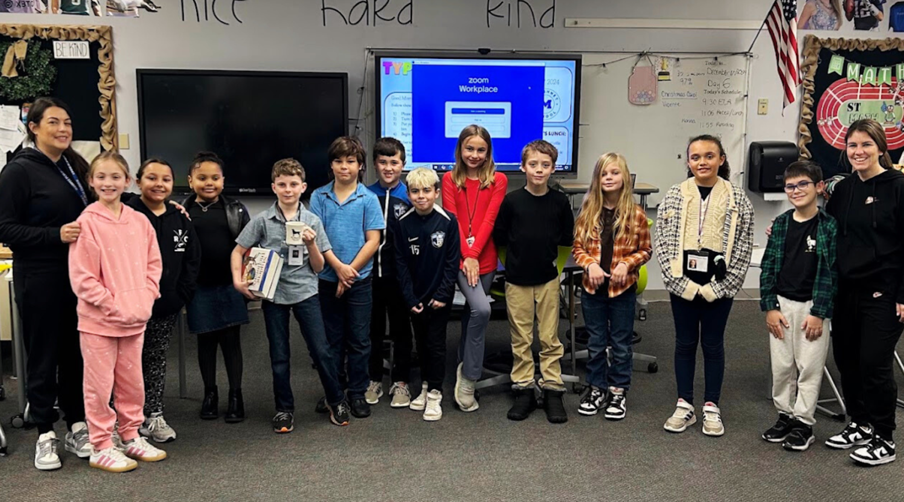 Students posing together in a classroom with digital screens behind them.
