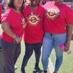 Three women in red shirts with colorful logos stand together outdoors.