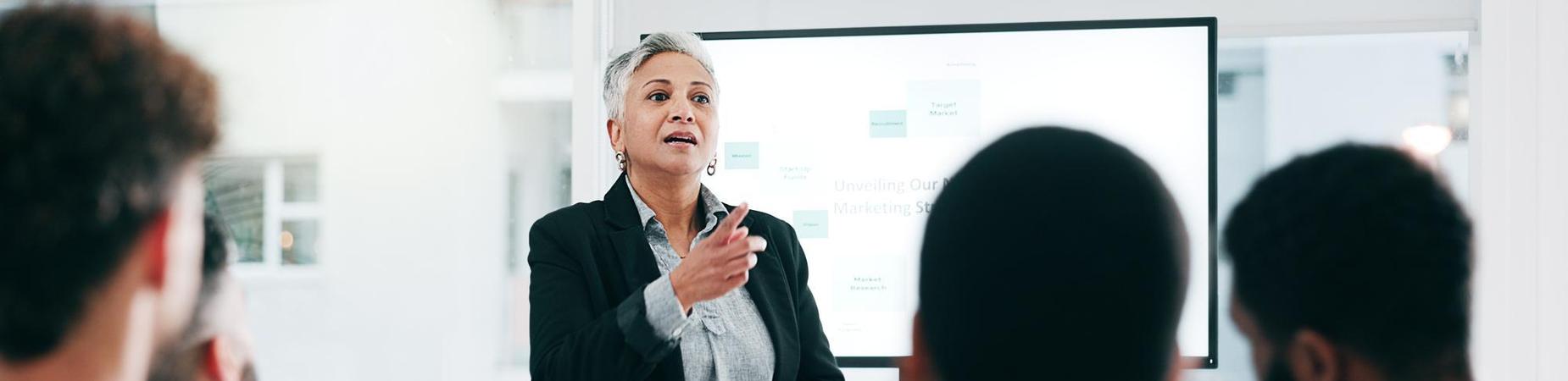 Professional looking woman lecturing to adults in training classroom.