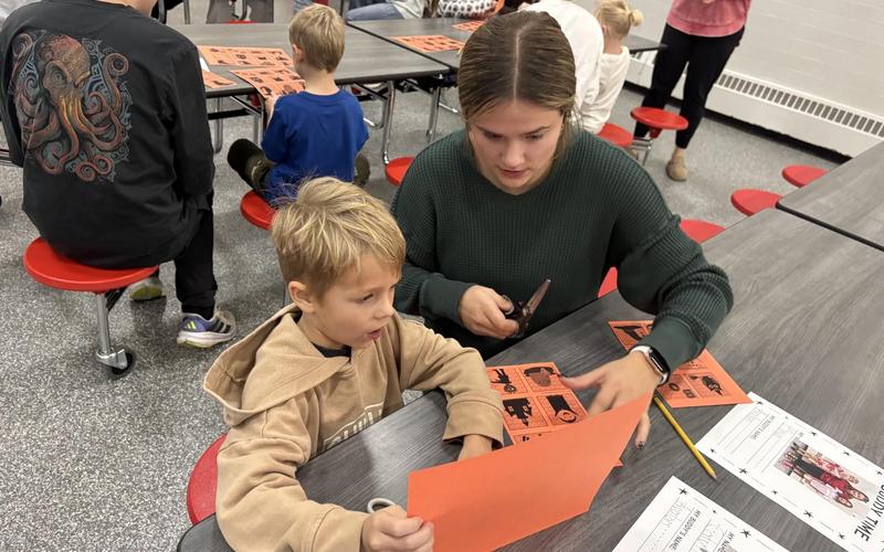 A young child and a teenager work together on a craft project at a table.