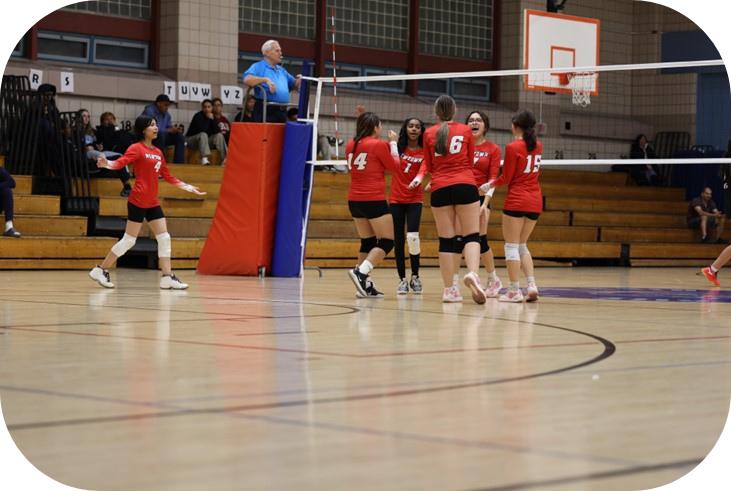 Girls Varsity team in action. Six female students in Newtown Volleyball uniform cheering in front of a volleyball net.