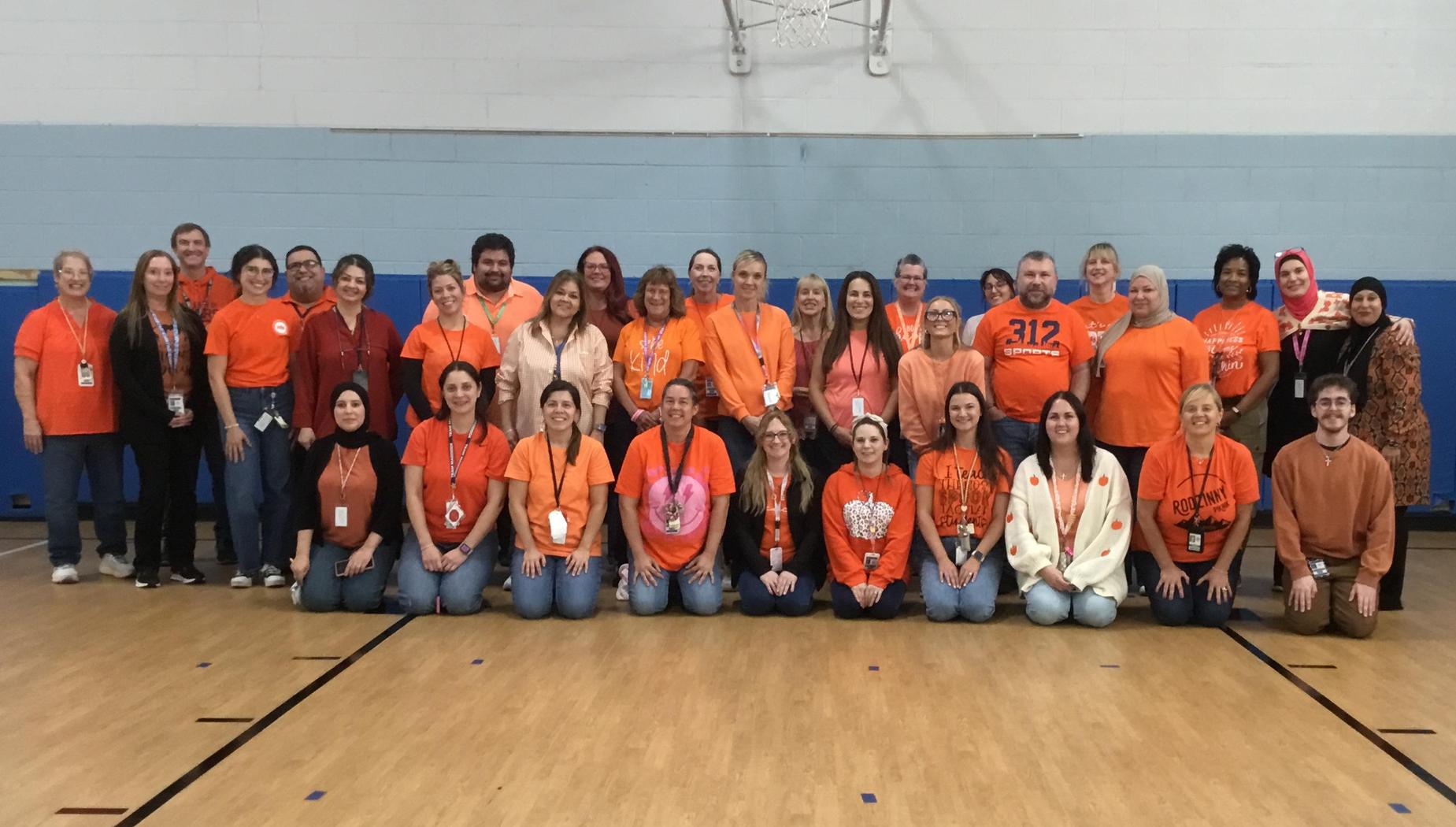Group of people wearing orange shirts posing together in a gymnasium.