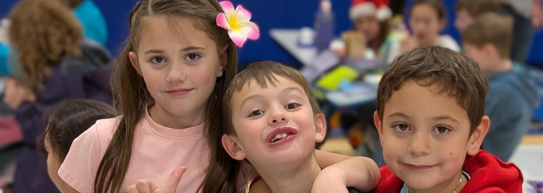 Three children sharing a playful moment in a gym, wearing colorful outfits.