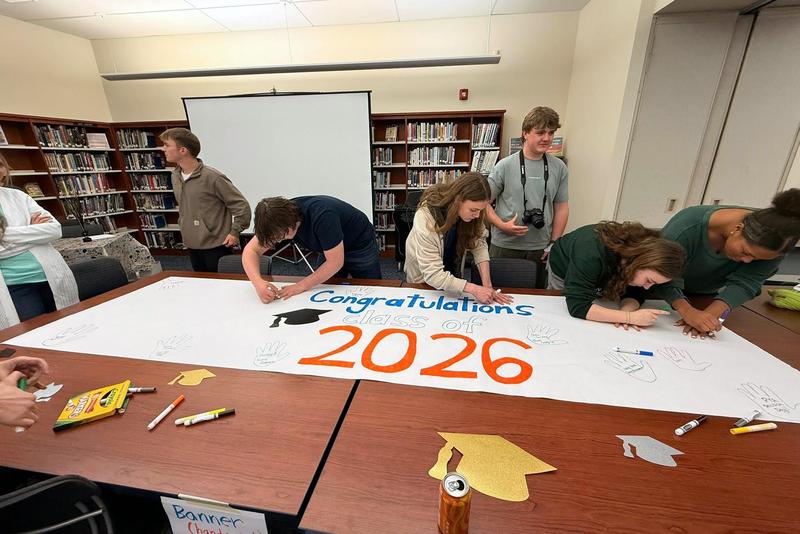 A group of students sign a large sheet of paper that says 