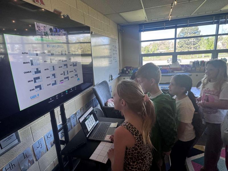 Deeply engaged third graders in a school classroom work to crack codes during a virtual satellite-repair simulation