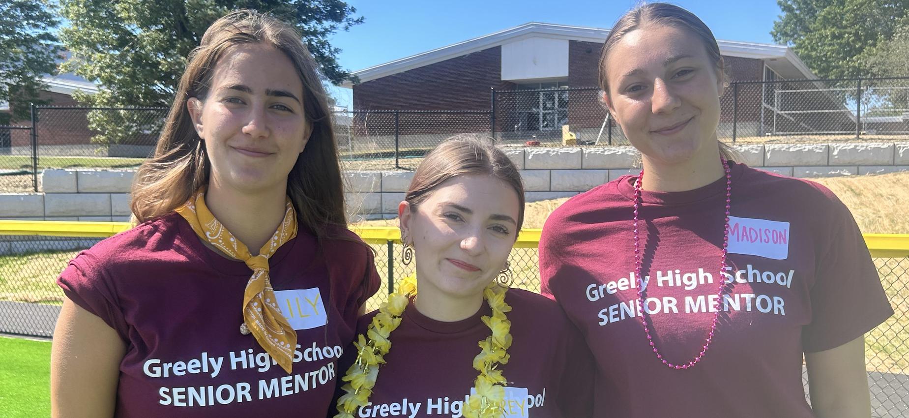 Three women wearing matching maroon t-shirts with 'Senior Mentor' standing outdoors.