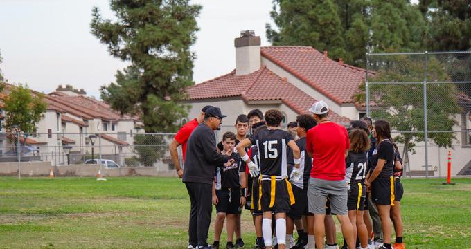 Group of young athletes gathered for instructions on a sports field.