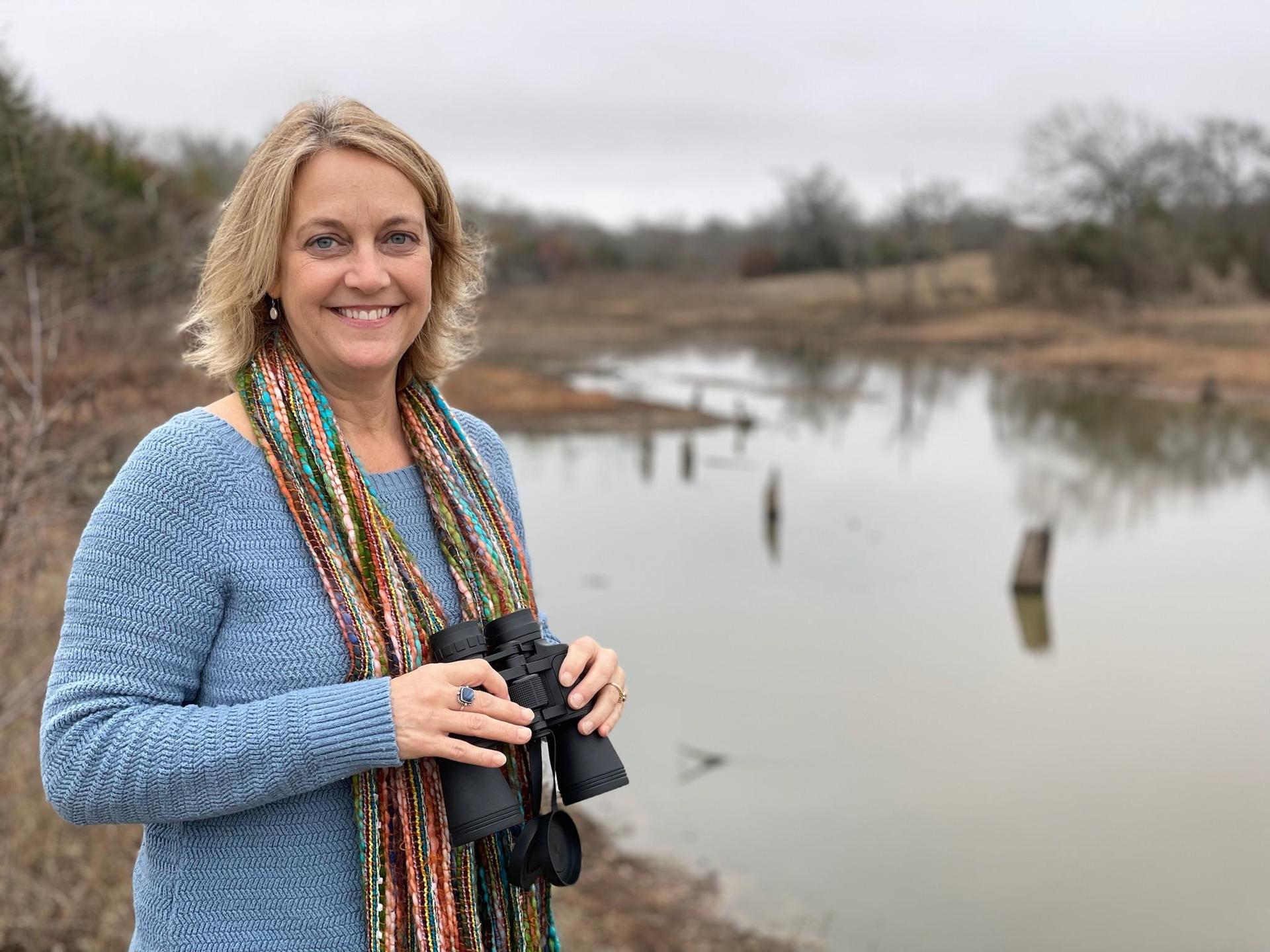 Mrs. Lagueux standing in front of a pond with binoculars