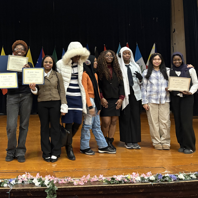 CMSA Speech and Debate students stand on a stage holding awards and certificates after a debate tournament.
