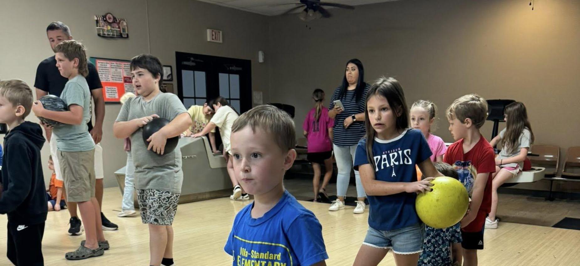 A young boy standing with a puzzled expression, others playing in the background.