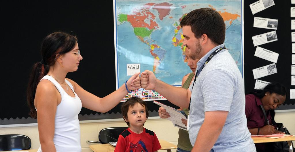 A teacher greets a student with a fist bump.