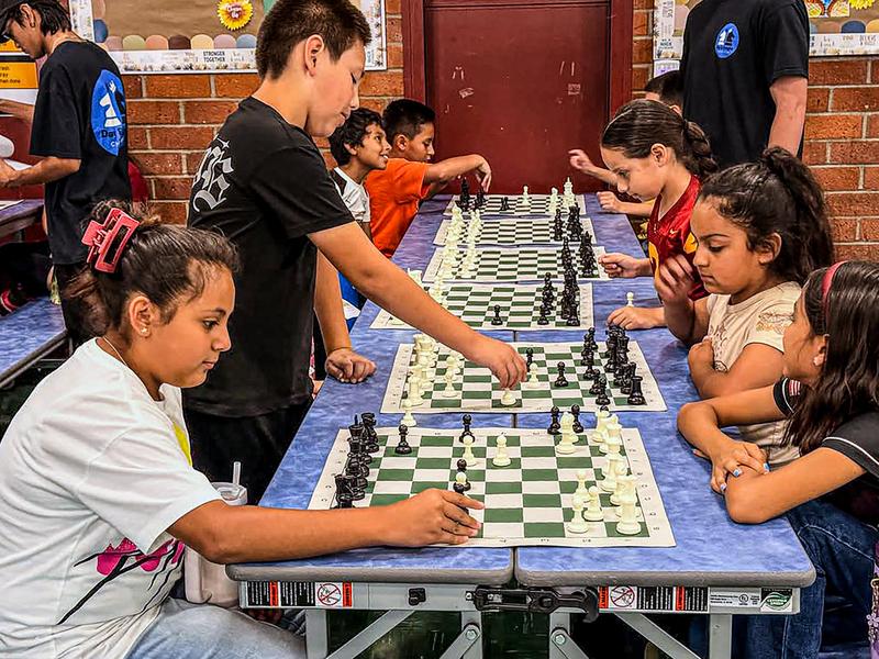 about 12 students playing chess with 2 of them being moderators or teachers