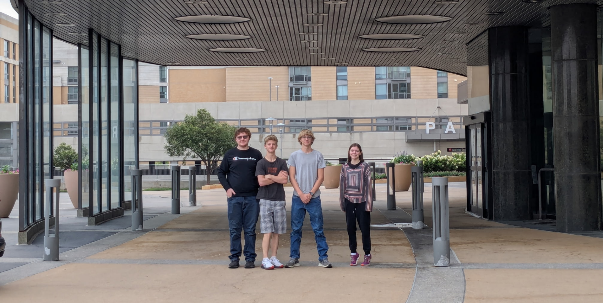 Four teenagers posing together under a modern building structure.