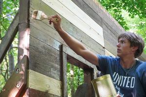 Frank Wilkinson reaches high to help stain some outdoor play items at a camp.