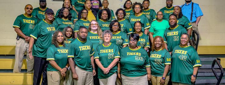 Group of people wearing green shirts with 'TIGERS' printed, standing in a staircase.
