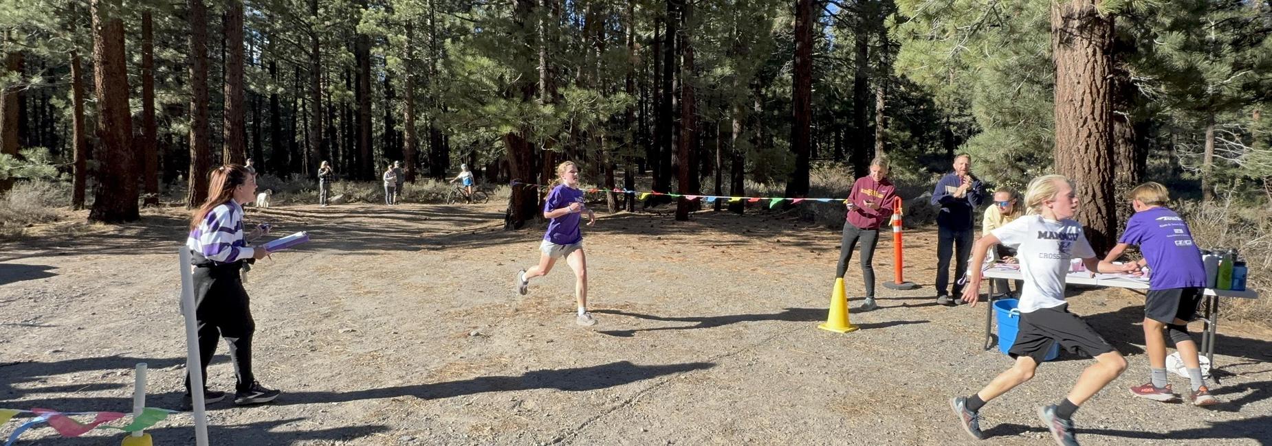 Runners participating in a forest race with volunteers cheering and directing them.