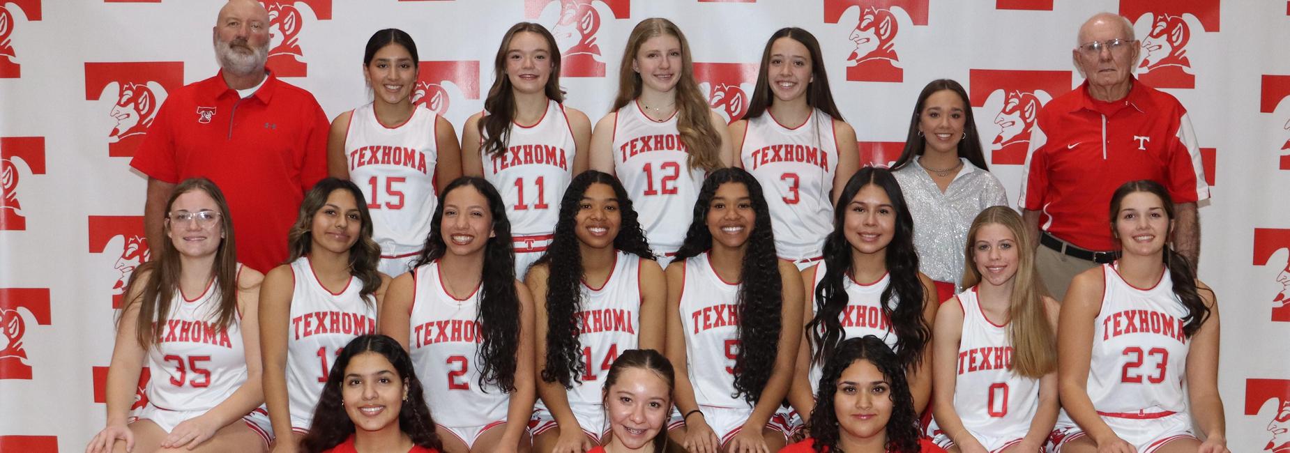 Girls basketball team posing for a group photo with players in jerseys and a red shirt in front.