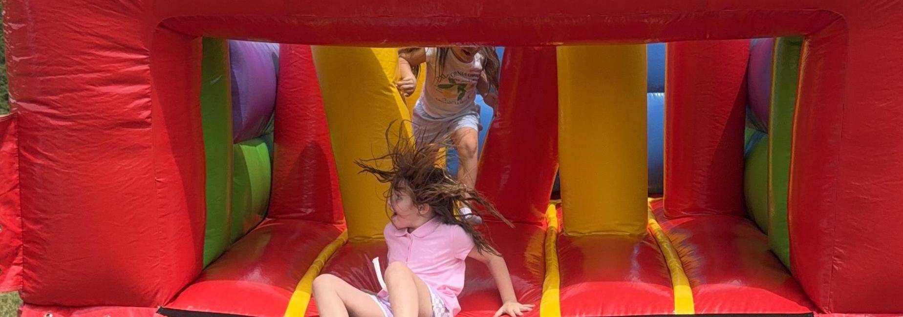 Children playing on a colorful bouncy castle, one sliding down and another jumping.