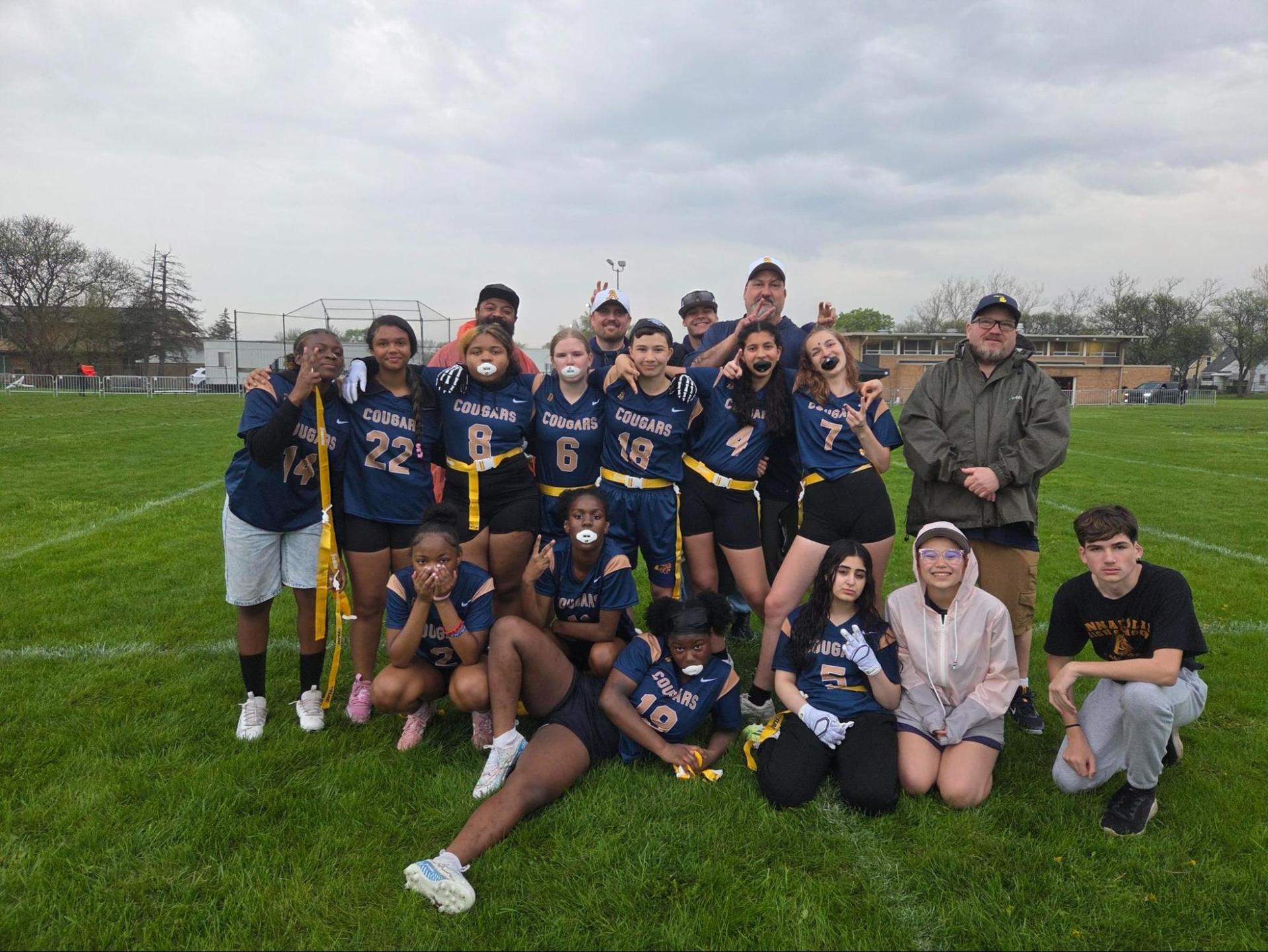 Youth sports team posing on a grassy field with coaches and players.