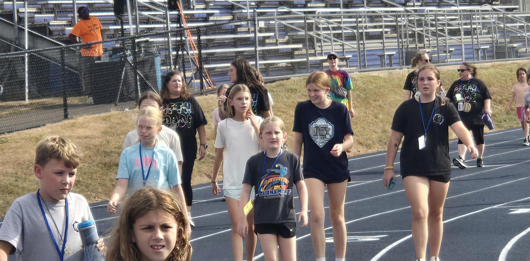 A mixed group of girls and boys, some talking and walking on a track at an event.