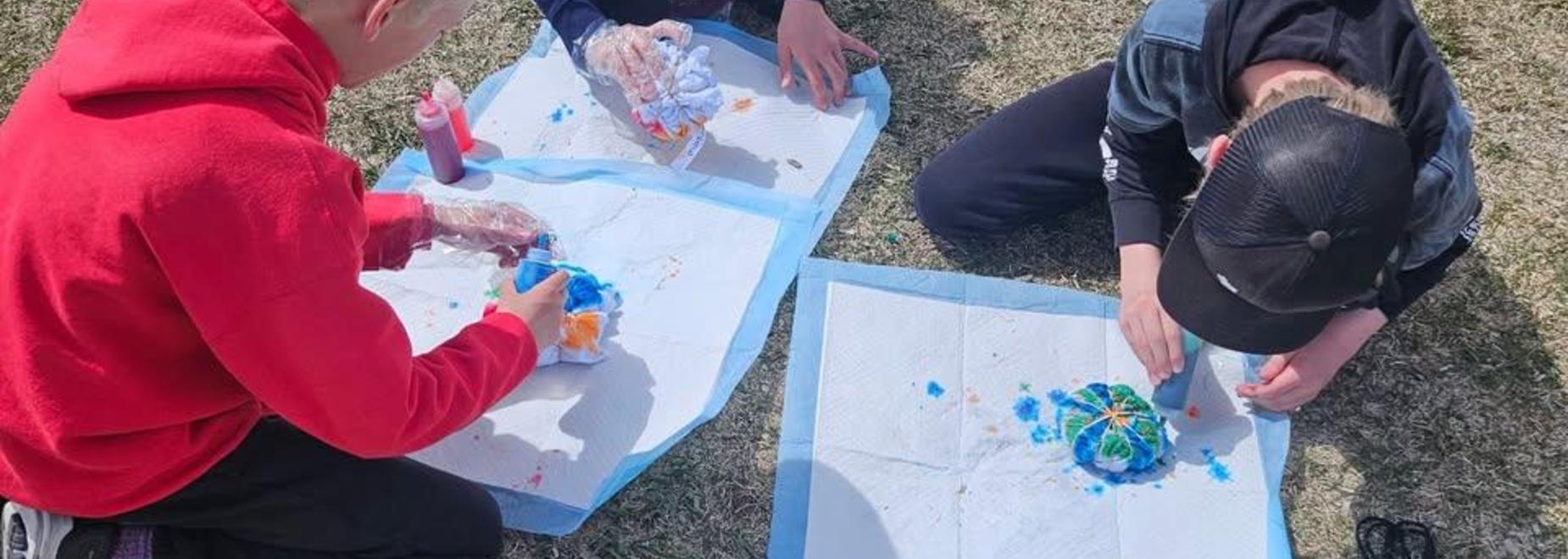 Children creating colorful art while sitting on the grass.
