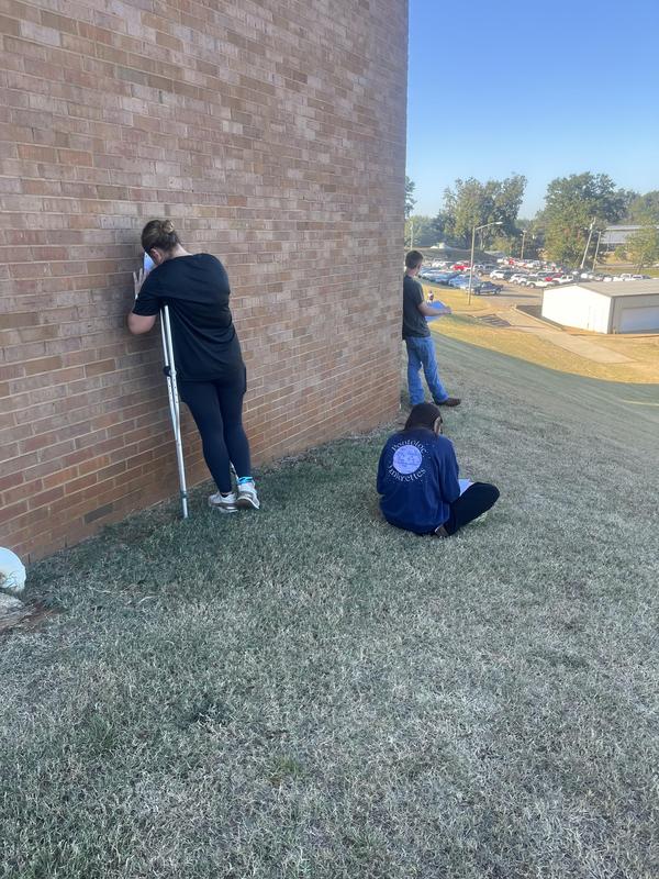 students standing up behind the library's back wall, writing
