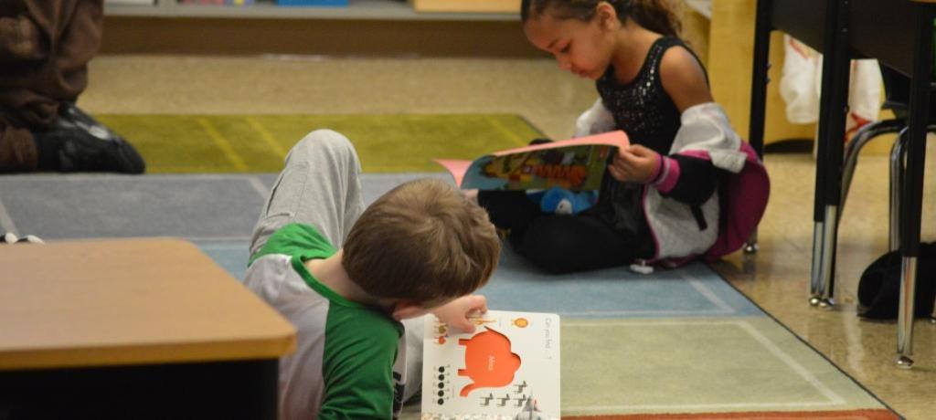 2 students sit on rug reading books