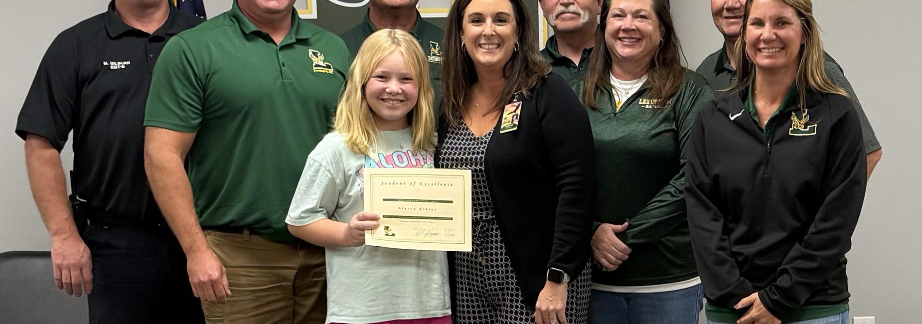 Group of people posing with a girl holding a certificate of excellence.