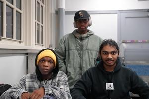 Three young men sitting together, two looking directly at the camera.