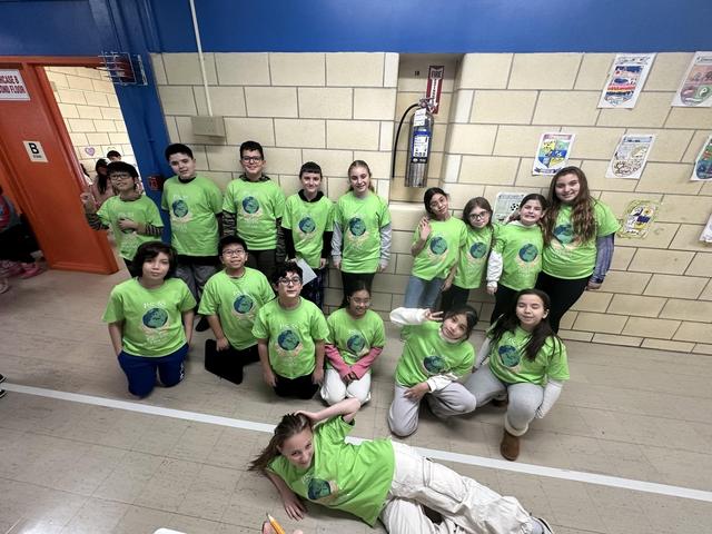 Group of students in green shirts posing together in a school hallway.