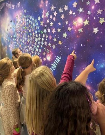 Children pointing at a wall decorated with stars in a cosmic design.