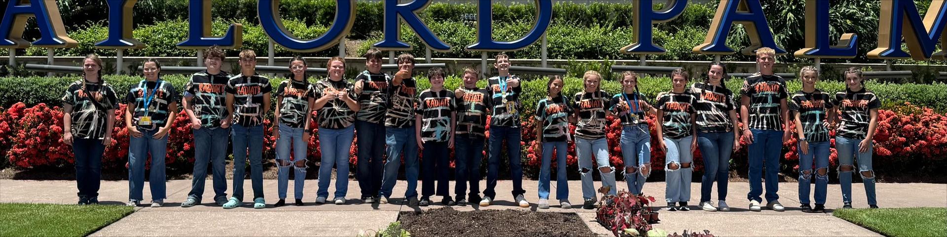 Group of students standing in front of flowers and plants acting silly.  