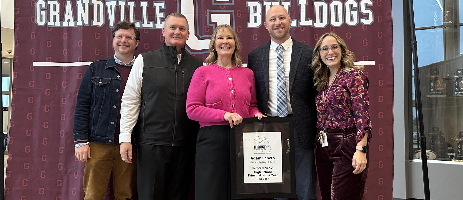 5 adults stand in front of Grandville themed backdrop with a woman holding a plaque