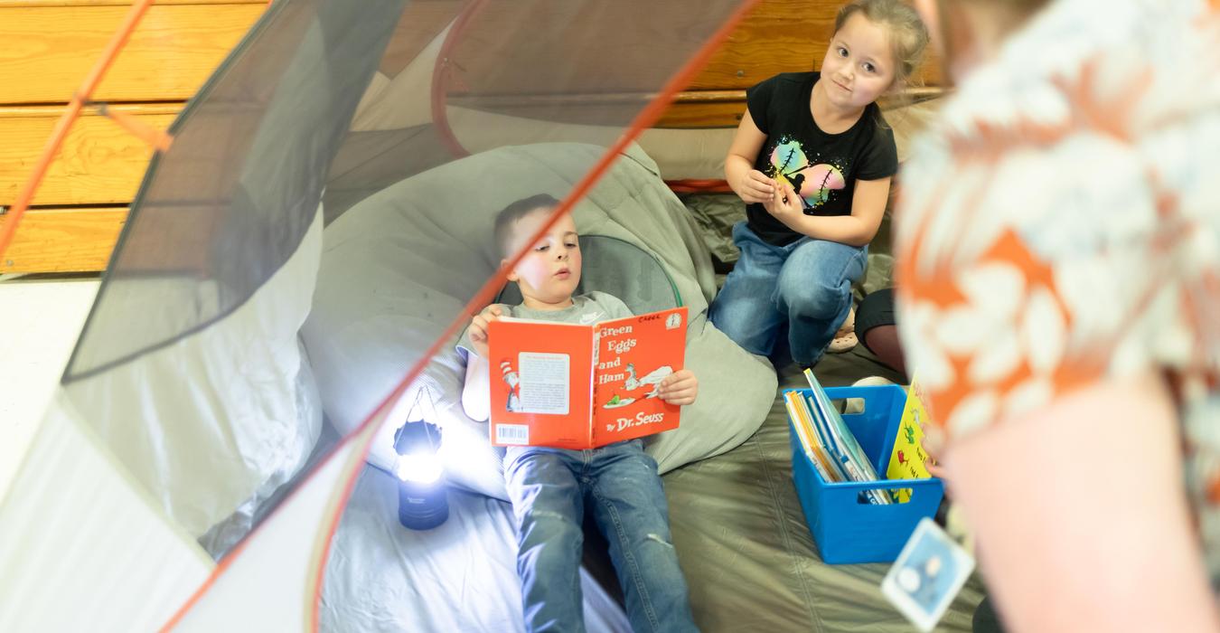 Child reading a book under a tent with a lantern.