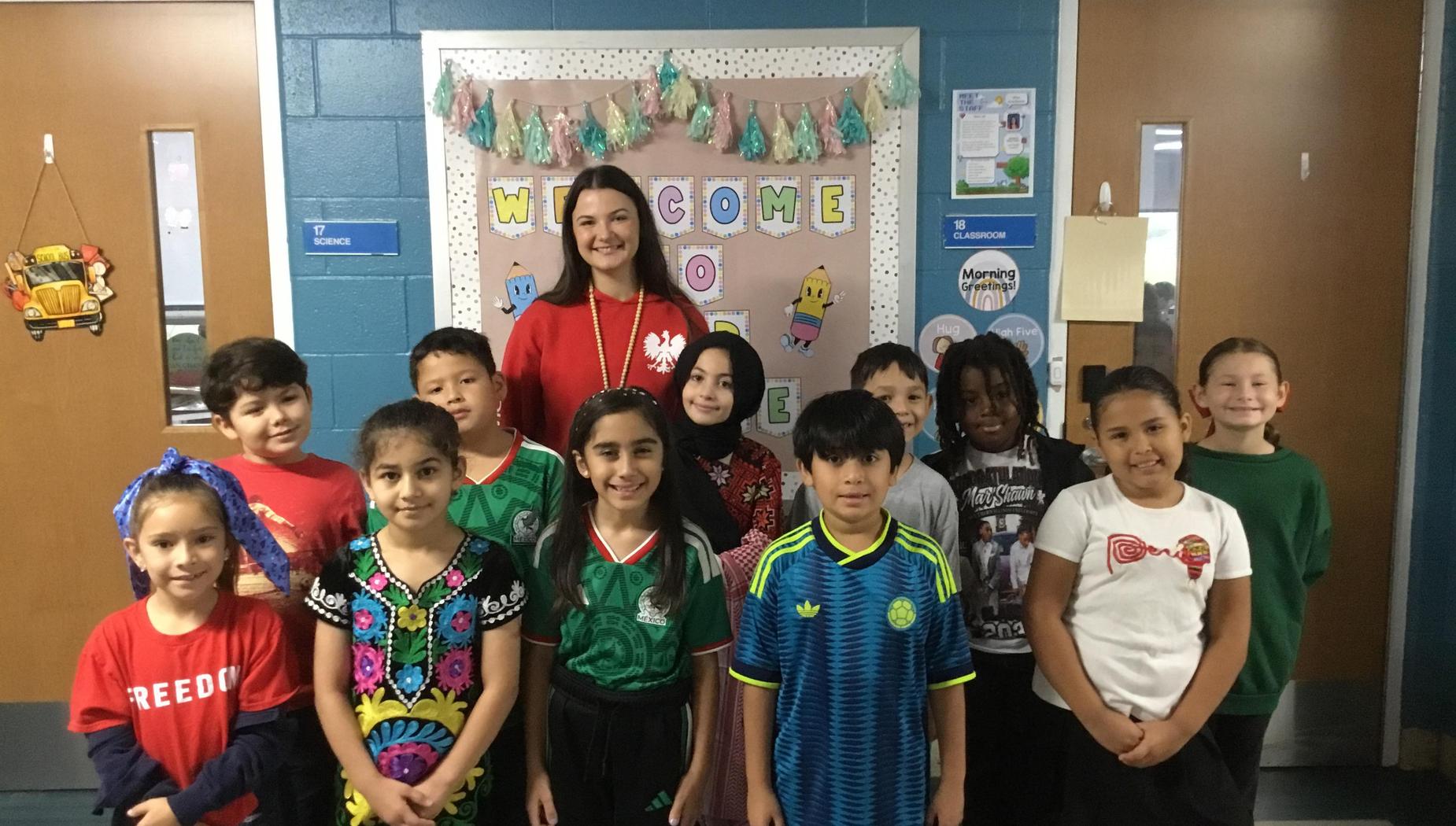 A group of twelve children and a teacher, all wearing colorful attire in a school setting.