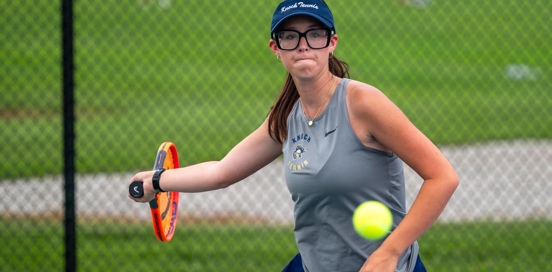 A girl playing tennis, wearing glasses and preparing to hit a ball with a racket.