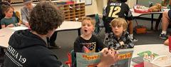 A student reading a book to captivated young children in a classroom.