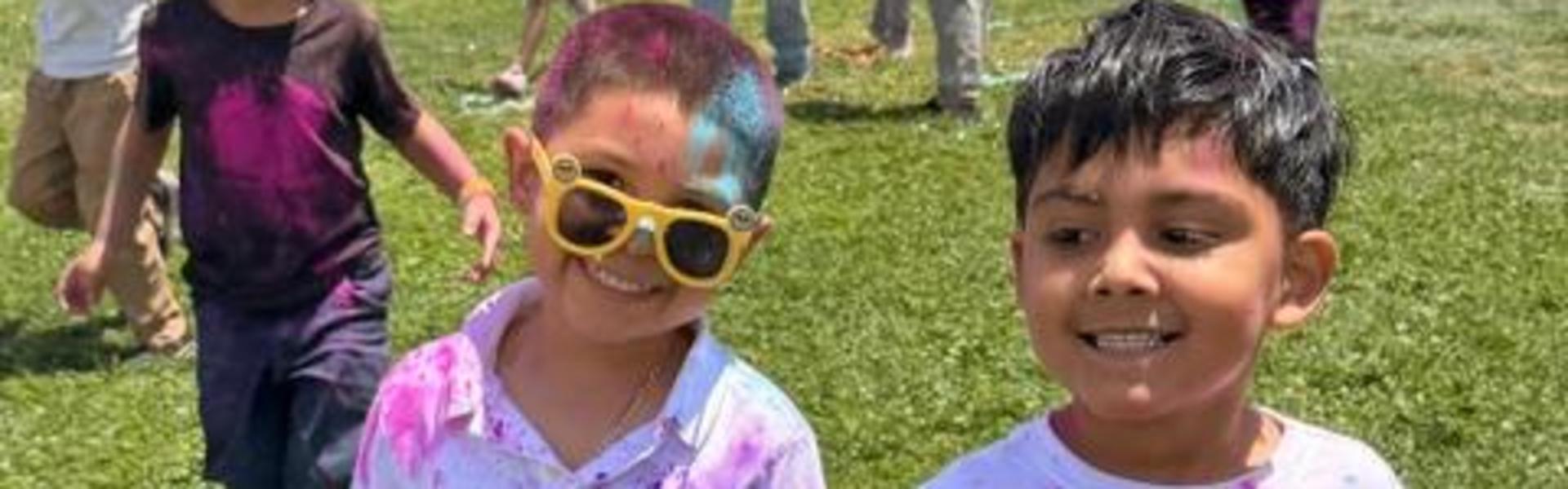 Two children holding hands, wearing white shirts with pink paint stains.