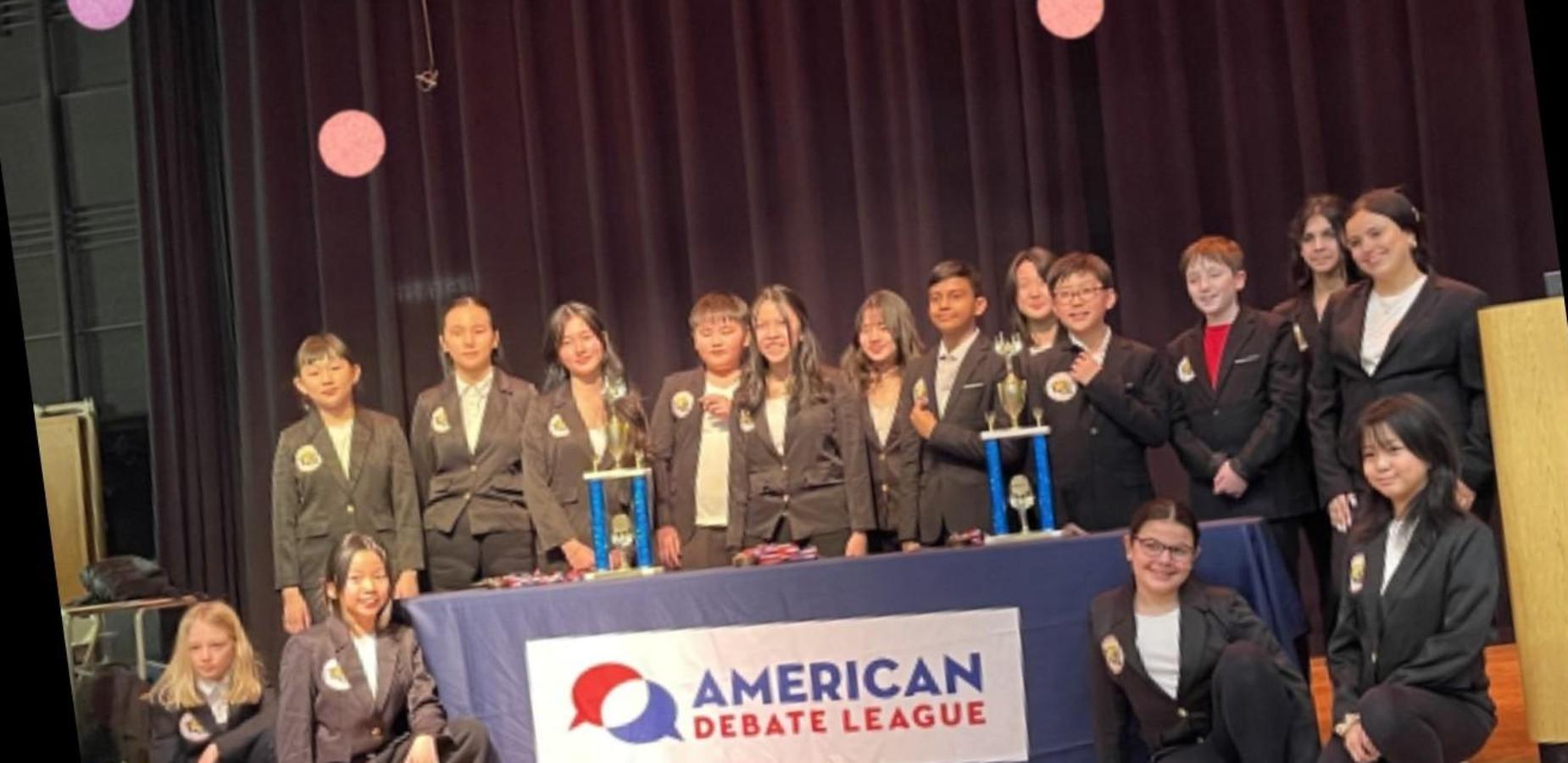 Group of students in formal attire at a debate event with trophies.