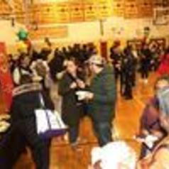 A crowded gym with people socializing and balloons in the background.