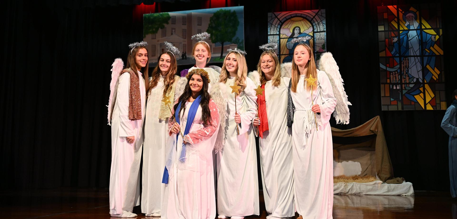 A group of girls dressed as angels on a stage, posing for a photo.