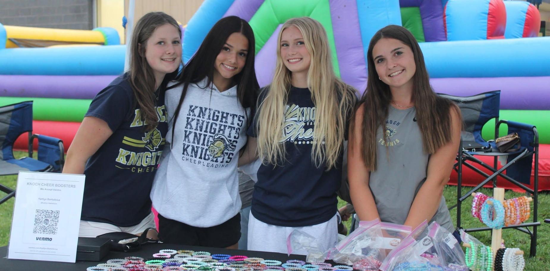 Four girls at a booth with merchandise, smiling and posing for the camera.