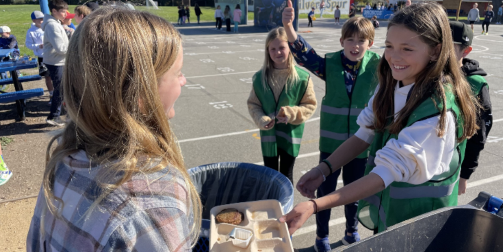 Students in green vests help dispose of trash during a school event.