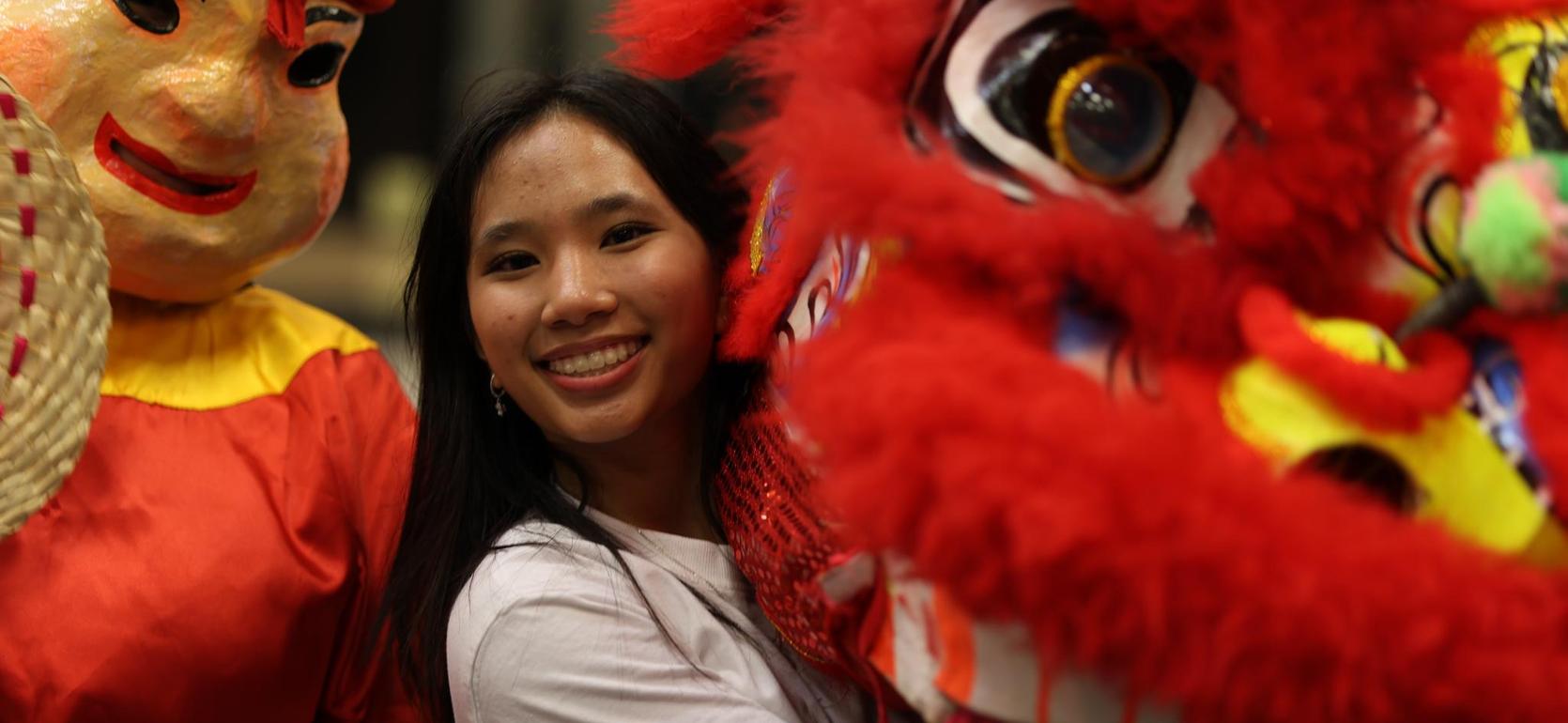 Young woman smiling while posing with a vibrant lion dance costume.
