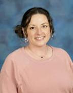 Blonde headed woman standing in front of a bush.