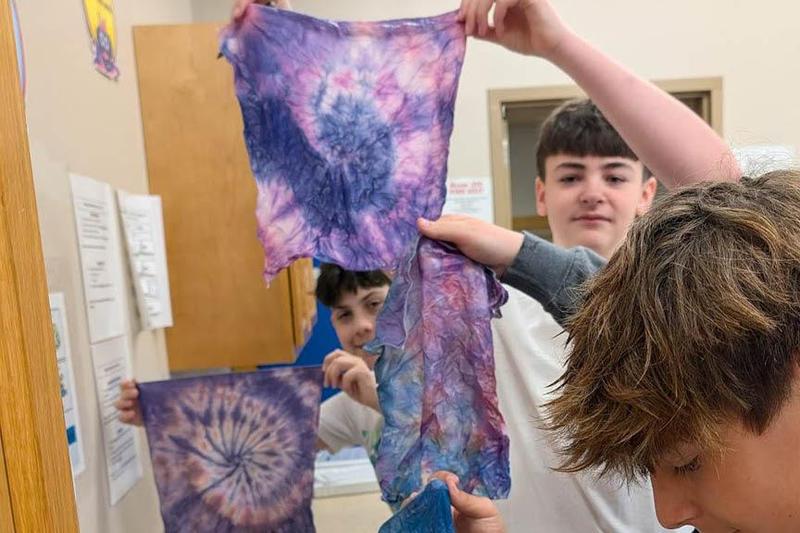 Students unroll their fabric squares to reveal the colorful designs