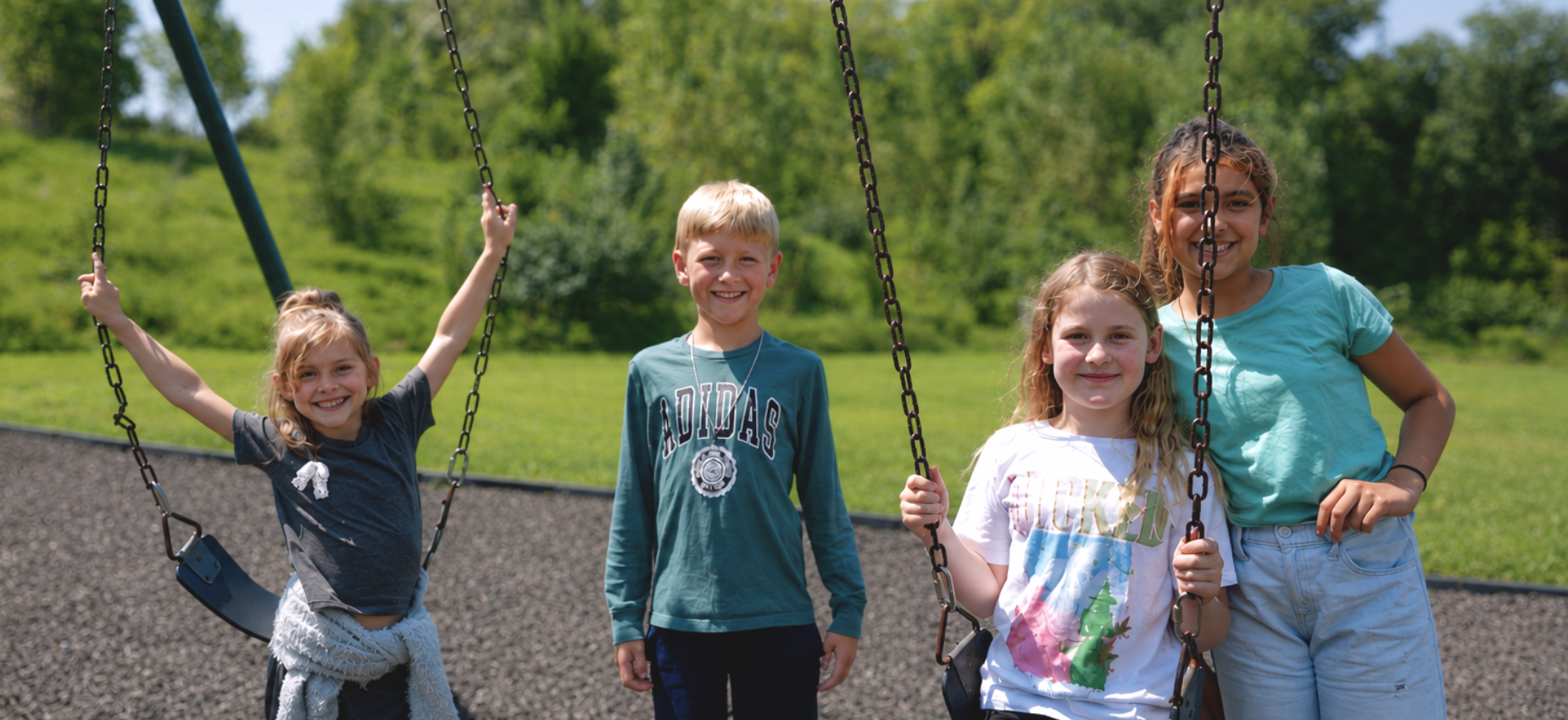 Four children pose on swings at a playground.