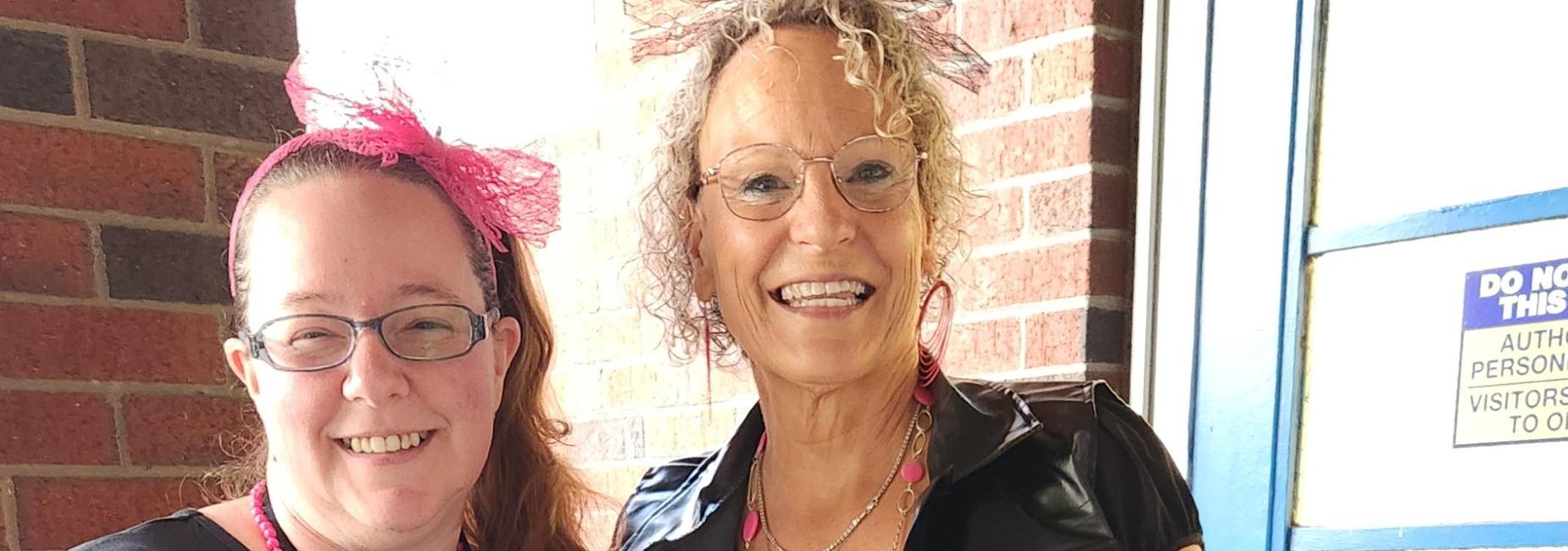 Two adults in pink-themed outfits, one with a zebra print skirt and leggings, smiling for the camera.