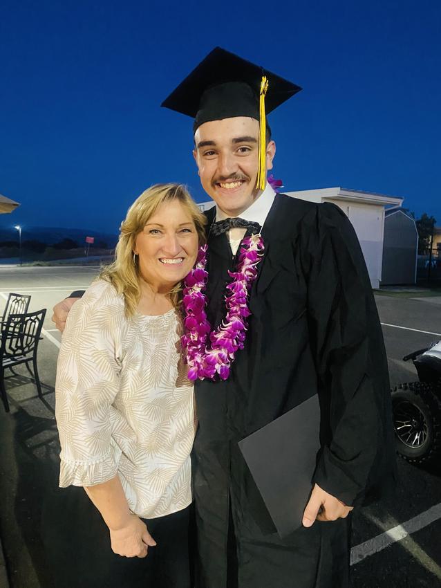Man in graduation attire with a floral lei posing with a smiling woman.